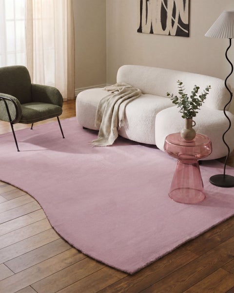 Moderner Wohnraum mit hellem Bouclé-Sofa, grünem Sessel und einem großen, wellenförmigen Teppich auf Echtholzparkett.