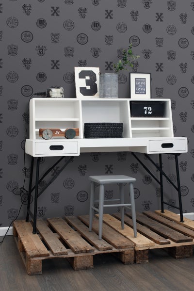 Szene mit weißem Schreibtisch, Hocker und Holzpalette vor einer grauen Wand mit Muster