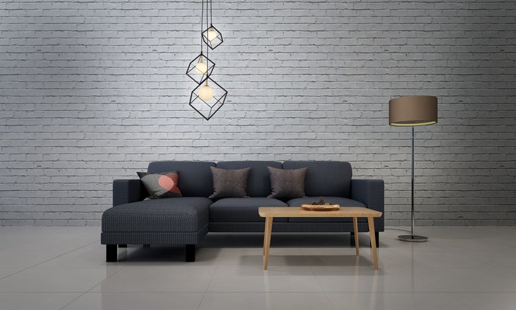 Wohnzimmer mit Ecksofa, Holztisch, Stehlampe und Hängelampe vor einer Backsteinwand