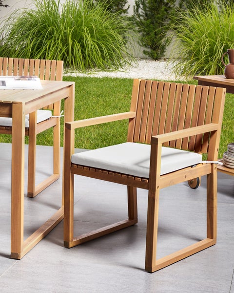 Moderner Gartenstuhl aus Holz mit weißem Sitzkissen und Rückenlehne in Lattenoptik auf einer Terrasse.