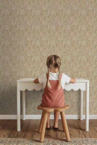 Kind sitzt an einem Tisch vor einer floralen Tapete.