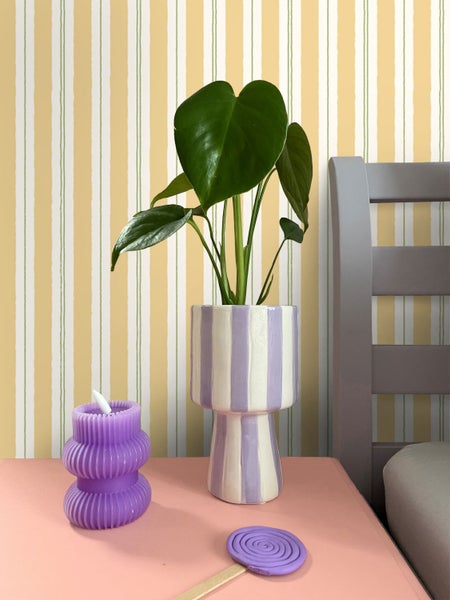 Zimmer mit Pflanze in gestreiftem Topf, gewellter Kerze und Lollipop-Dekoration