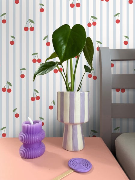 Dekorative Szene mit Pflanze im gestreiften Übertopf, Kerze und Dekoration auf einem Nachttisch