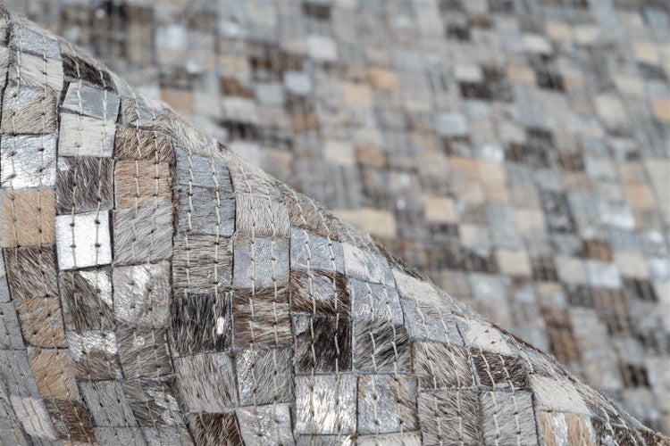 Nahaufnahme eines Patchwork-Teppichs aus quadratischen Fellstücken mit Metallic-Effekt und sichtbaren Nähten.