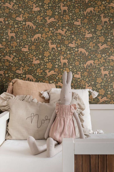 Tapete mit Reh und Blumen Muster in einem gemütlichen Kinderzimmer mit Kissen und Stofftier auf einem weißen Bett.