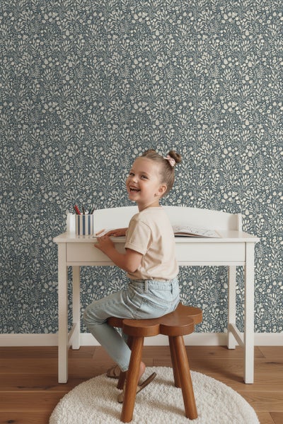 Mädchen am Schreibtisch vor einer Wandtapete mit floralem Muster