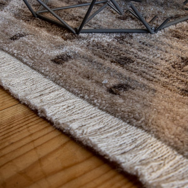 Nahaufnahme eines gemusterten Teppichs mit Fransen auf einem Holzboden unter einem geometrischen Metallgestell.