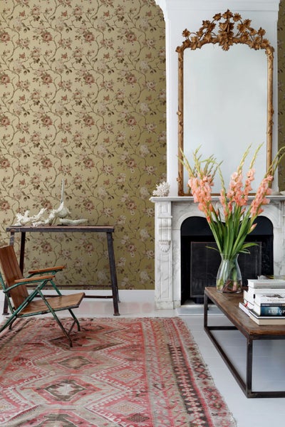 Wohnzimmer mit Blumentapete, antikem Spiegel über dem Kamin und gemustertem Teppich.