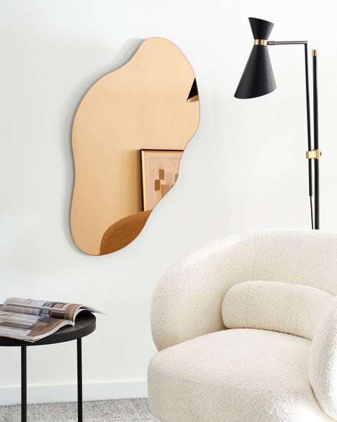 Wohnzimmerszene mit einem unregelmäßig geformten Spiegel, einer Stehlampe und einem Sessel.