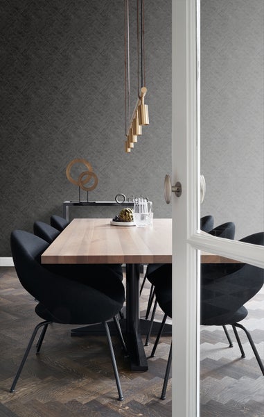 Esszimmer mit Holztisch, schwarzen Stühlen und goldener Hängelampe vor einer gemusterten Tapete.