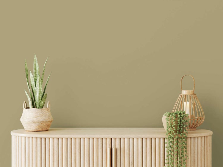 Helles Sideboard aus Holz vor einer olivgrünen Wand mit einer Zimmerpflanze im Korb und einer dekorativen Laterne aus Bambus.