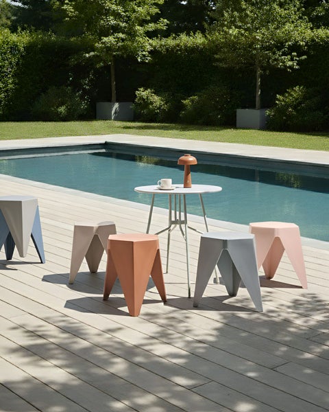 Modernes Gartenmöbel-Set mit geometrischen Hockern und einem runden Tisch auf einer hellen Holzterrasse neben einem Swimmingpool.