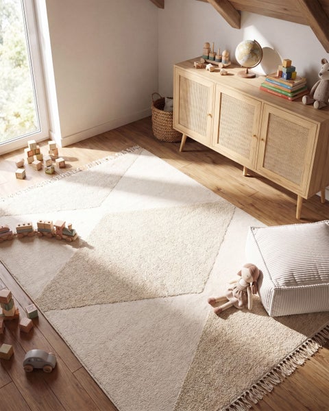 Ein helles Kinderzimmer mit einem strukturierten Teppich mit geometrischem Muster, einer Anrichte aus Holz mit Rattantüren und Spielzeug.