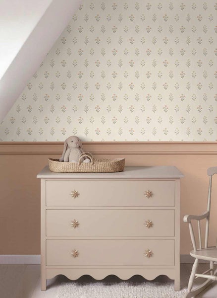 Vliestapete mit Blumenmuster in einem hellen Kinderzimmer über einer Kommode mit Sternengriffen und einem Stofftier in einem Korb.