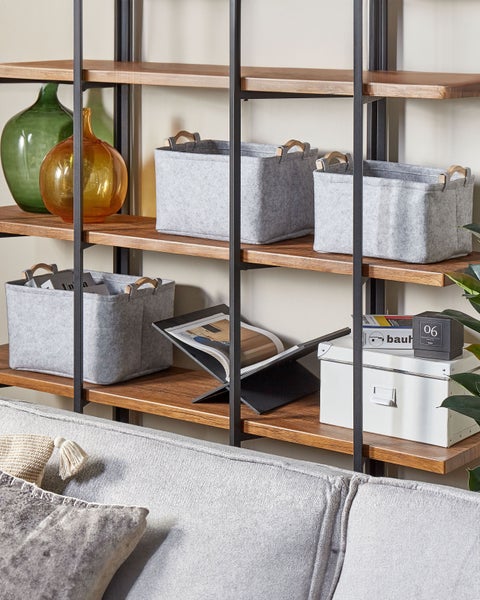 Offenes Regal aus Metall und Holz mit grauen Filzboxen und Glasvasen in einem hellen, organisierten Wohnzimmer.