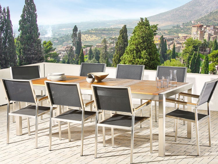 Modernes, helles Gartenmöbel-Set aus Edelstahl und Holz auf einer Terrasse, mit einem großen Esstisch und Stapelstühlen mit dunklem Netzgewebe.