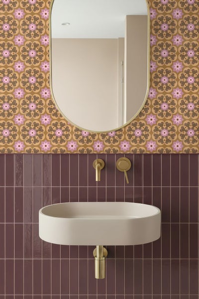 Modernes, organisiertes Badezimmer mit beigem Aufsatzbecken, goldener Wandarmatur, bordeauxroten Fliesen und floral gemusterter Tapete.