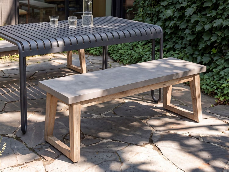 Gartenbank mit Betonoptik Sitzfläche und Holzbeinen auf einer Steinterrasse neben einem Gartentisch.