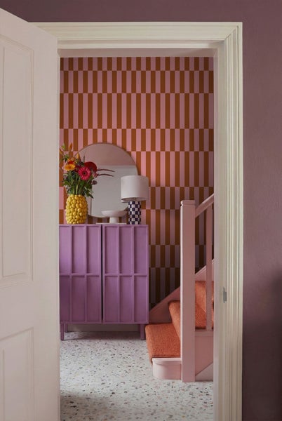 Blick durch eine offene Tür auf eine Inneneinrichtung mit Kommode, Spiegel und Treppe