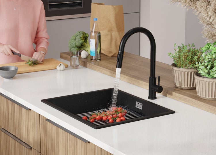 Küchenszene mit schwarzem Spülbecken, Armatur und Person, die Gemüse schneidet