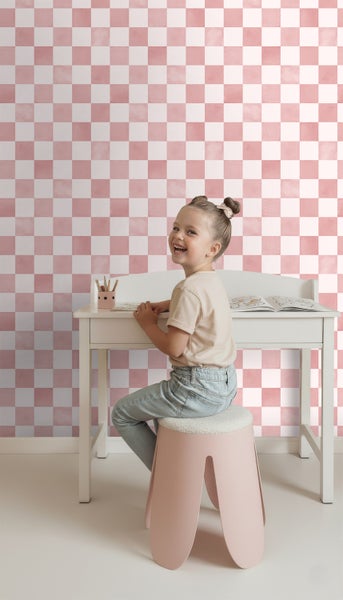 Mädchen sitzt an einem Schreibtisch vor einer Wand mit Schachbrettmuster-Tapete