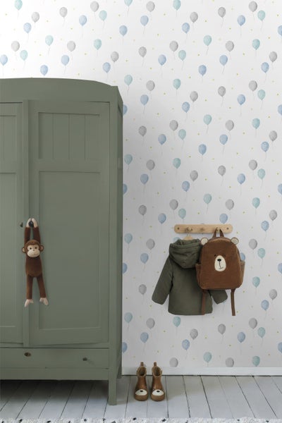 Kinderzimmer mit grünem Holzschrank und Spielzeugaffe, Tapete mit Ballonmuster, Wandgarderobe mit Jacke und Bärenrucksack sowie Stiefeln auf dem Boden.