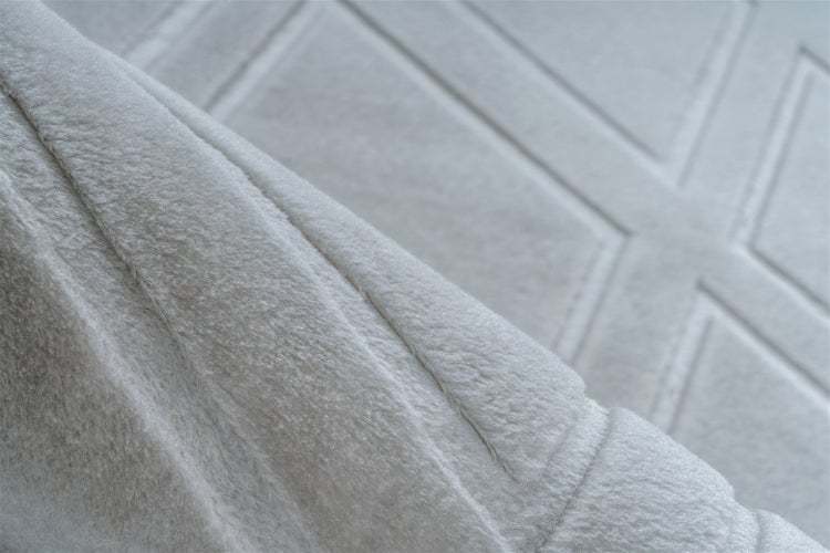 Detailaufnahme eines weichen Plüschteppichs mit geometrischem Linienmuster.