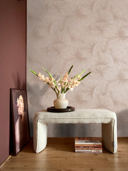 Innenraum mit gemusterter Tapete, gepolsterter Bank, Vase mit Blumen und einem gerahmten Bild