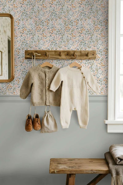 Tapete mit floralem Muster in einem Kinderzimmer mit einer Holzgarderobe und hängender Babykleidung vor einer Wandpaneele.
