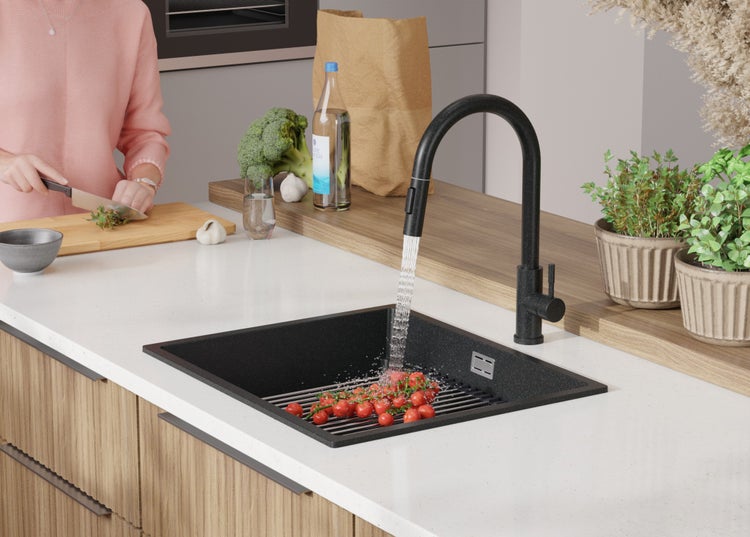 Schwarze Küchenspüle mit Wasserhahn in einer modernen Küche, auf der eine Person Zutaten zubereitet