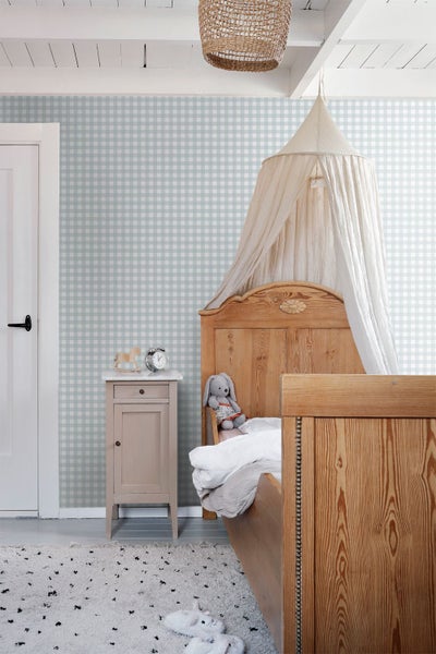 Hellblau-weiß karierte Tapete in einem gemütlichen Kinderzimmer mit Holzbett, Betthimmel und Nachttisch.
