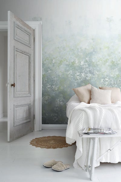 Helles Schlafzimmer mit floraler Tapete, offenstehender Holztür und weißer Bettwäsche