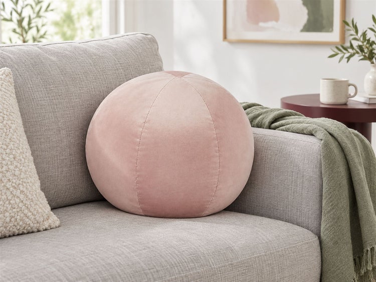 Rundes Dekokissen aus weichem Samt auf einem grauen Sofa platziert.