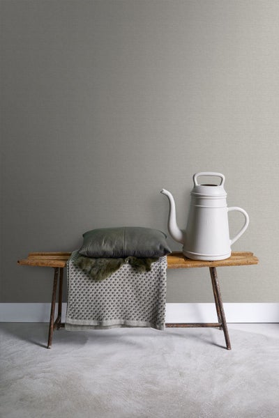 Dekorative Szene mit Bank, Kissen, Decke und Gießkanne vor einer Wand