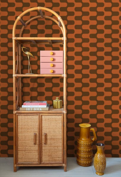 Retro-Tapete mit orange-braunem Wellenmuster hinter einem Rattanregal mit Dekorationsartikeln und Keramikvasen.