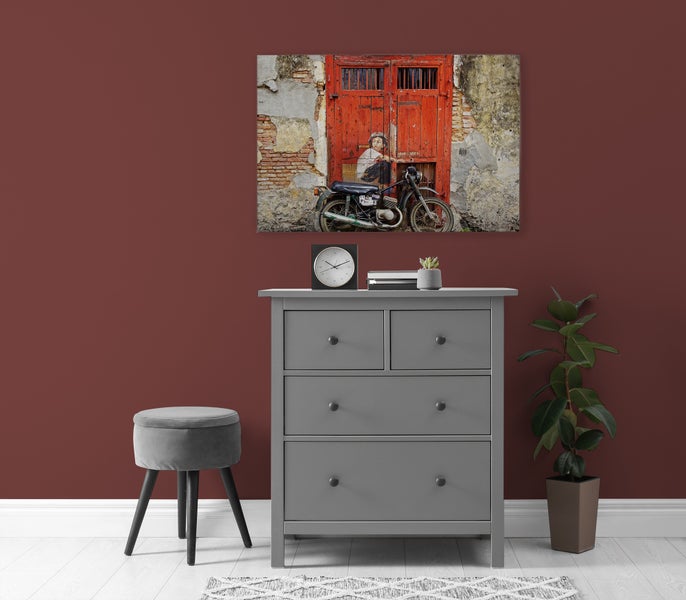 Eine Kommode aus Holz mit vier Schubladen steht vor einer Wand mit einem Wandbild eines Motorrads vor einer historischen Tür.
