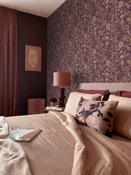 Dekoratives Schlafzimmer mit floraler Tapete, Textilien und Nachttischlampe