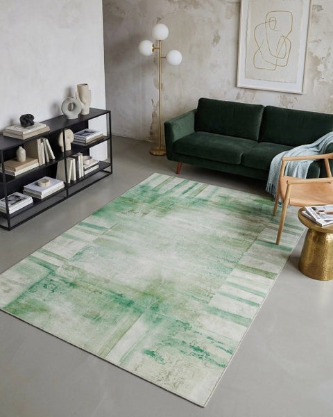 Modernes, helles Wohnzimmer mit abstraktem Teppich in Grün und Creme, grünem Samtsofa, schwarzem Metallregal und goldener Stehlampe.