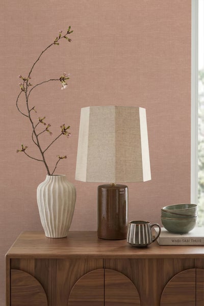 Strukturierte Tapete in Rosa hinter einem Holzsideboard mit Tischlampe, einer weißen Vase mit Kirschblütenzweig und Keramikschalen.
