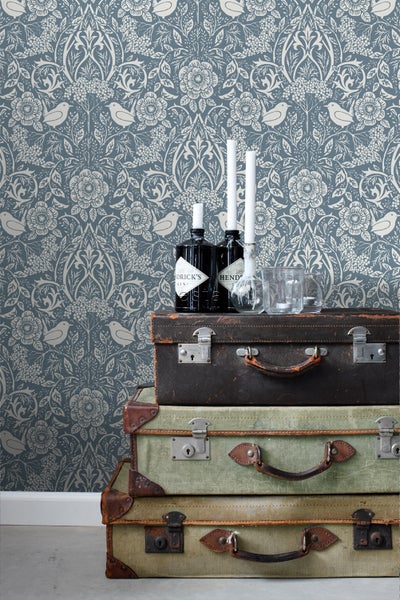 Dekorative Tapete mit Blumenmuster und Vogelmotiven über einem Stapel Vintage-Koffer