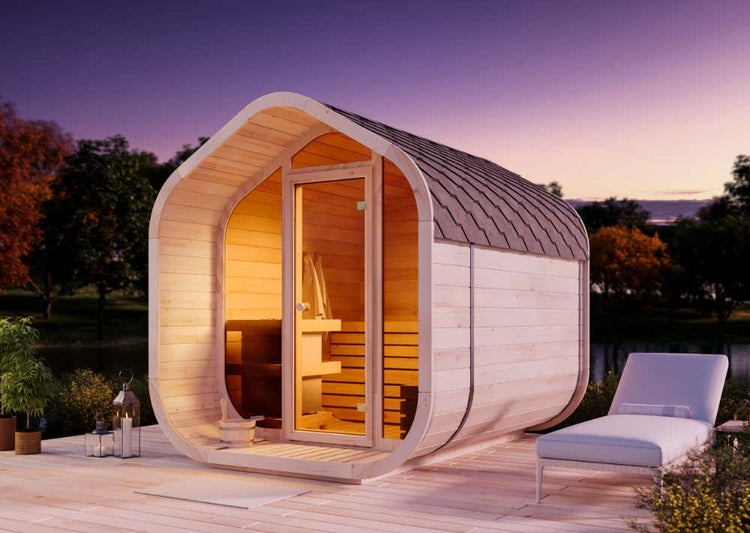 Abgerundete Gartensauna aus Holz mit Glastür auf einer Holzterrasse am See bei Abenddämmerung.
