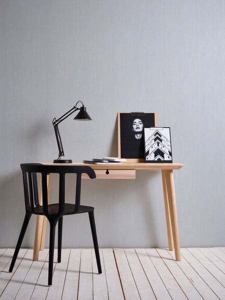 Ein heller Schreibtisch mit einer schwarzen Lampe, einer schwarzen Stuhl und Bildern an der Wand