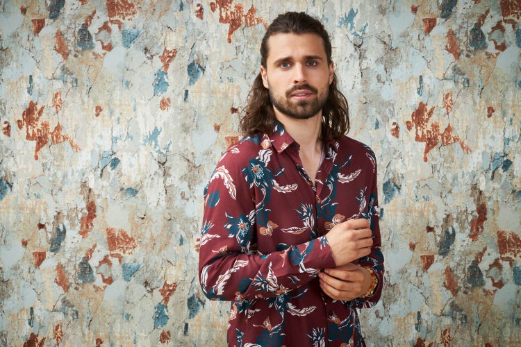 Schlafzimmer mit gemusterter Tapete, Holzbett und Zimmerpflanze im Korb