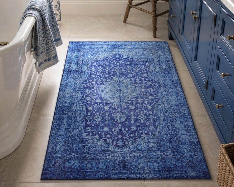 Rechteckiger Teppich mit blauem Orientmuster in einem Badezimmer zwischen Badewanne und Waschtischunterschrank.