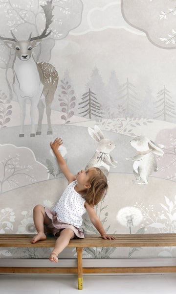 Mädchen sitzt vor einer illustrierten Tapete mit Waldmotiven, darunter Rehe und Hasen