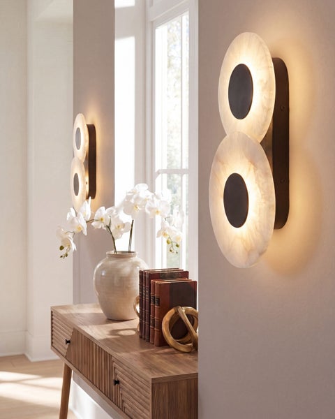 Zwei runde LED Wandleuchten mit alabasterartigem Schirm und zentralem Element in einem modern eingerichteten Flur mit Holzanrichte und Pflanzen.