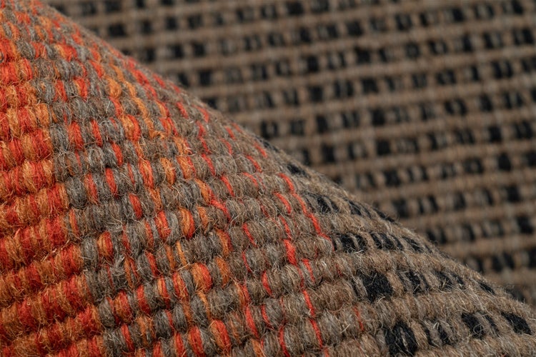 Nahaufnahme eines gewebten Teppichs in Orange, Braun und Schwarz mit grober Textur und Gittermuster.