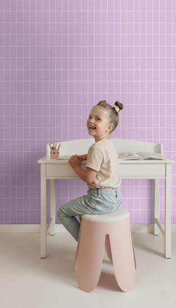 Mädchen sitzt an einem Kinderschreibtisch mit einem rosa Hocker und einer lila Wand im Hintergrund