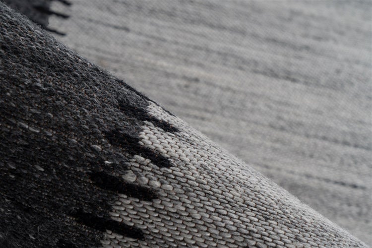 Nahaufnahme eines gewebten Teppichs mit grauem und dunkelgrauem geometrischem Muster und grober Textur.