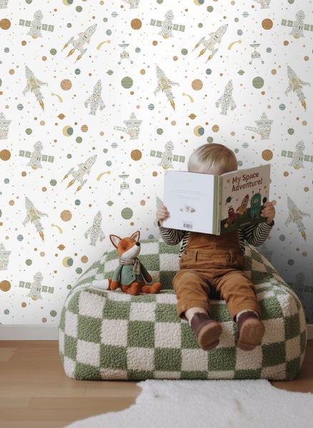 Kind liest ein Buch auf einem Sitzsack vor einer Kindertapete mit Weltraum-Motiven wie Raketen, Planeten und Satelliten.